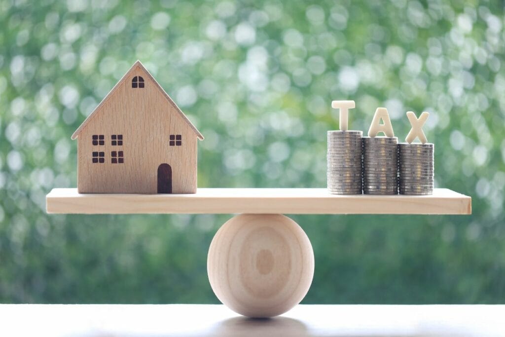 The model house with a stack of coin money and tax word on seesaw indicating tax on commercial property