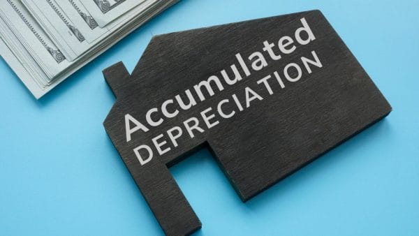 A wooden house-shaped sign reading 'Accumulated Depreciation' with stacks of money behind, symbolizing the financial concept in real estate.