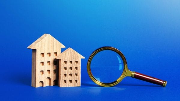 Wooden model houses next to a magnifying glass on a blue background, representing the analysis of 'is accumulated depreciation an asset' in property valuation.
