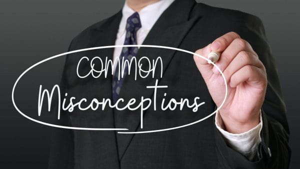 A person in a business suit writing the words "common misconceptions" on a clear surface with a marker, representing a theme of addressing common misunderstandings, potentially about financial metrics such as net operating income (NOI) in real estate.