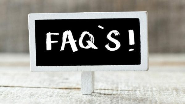 A small chalkboard sign stands on a wooden surface with "FAQ's" written in white chalk, suggesting a section dedicated to answering frequently asked questions about Net Operating Income (NOI) in real estate.