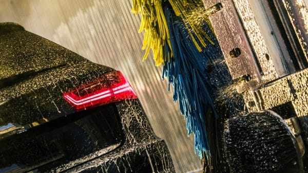 Close-up of a black car undergoing cleaning with yellow and blue brushes in a car wash, symbolizing the active business being discussed in a guide about how to effectively sell a car wash.