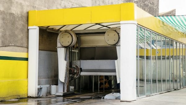 An image of an empty, slightly worn-out car wash station with yellow accents and clear glass walls, illustrating a guide on how to sell a car wash property.