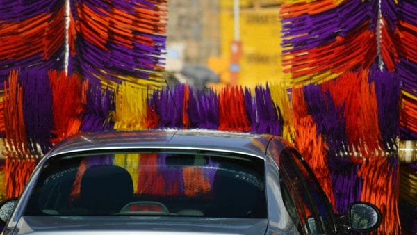  A car is shown mid-wash, surrounded by striking purple, orange, and yellow brushes of a car wash, serving as a vibrant visual for content on strategies for how to sell a car wash business.