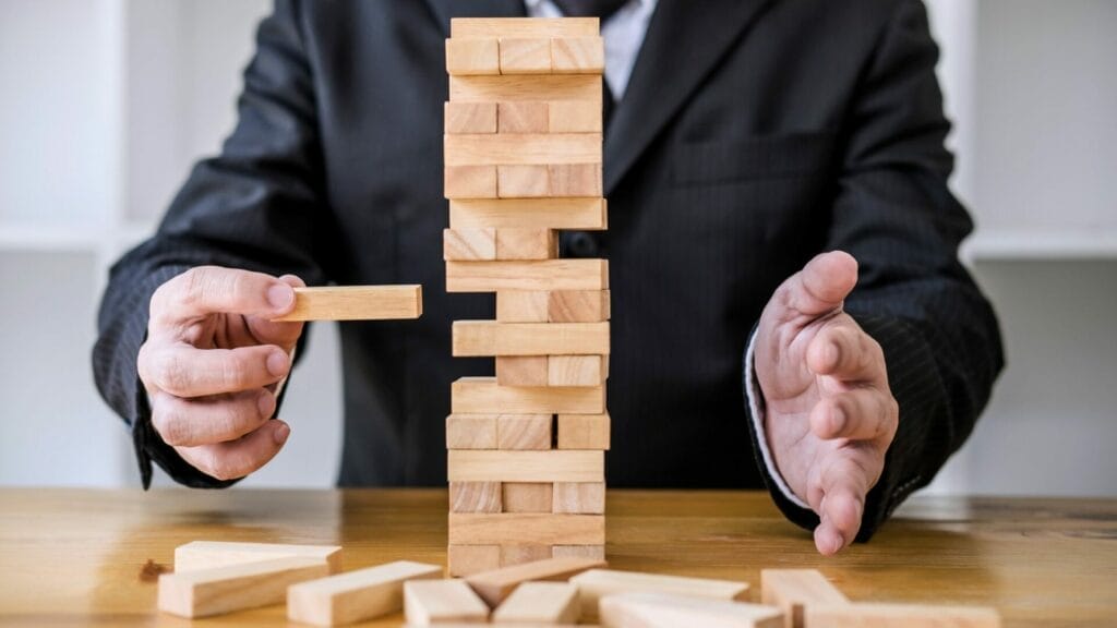 Image of a person in a business suit carefully extracting a block from a nearly complete tower in a game of Jenga, symbolizing strategic decision-making, featured in a blog post titled 'Seamless Sales with Point Acquisitions.' This represents the delicate balance and precision in navigating sales strategies in the business world.