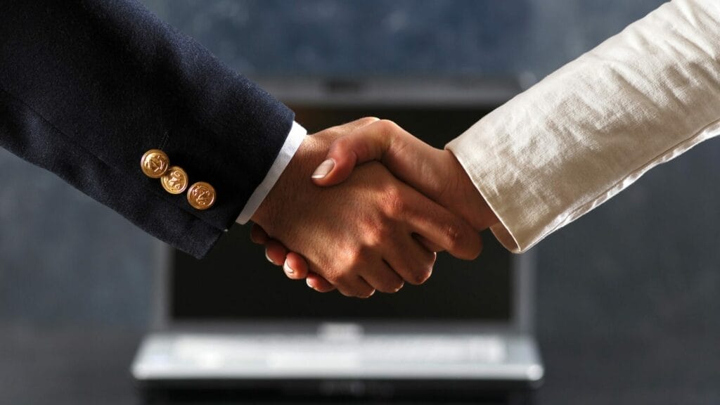 Close-up of a firm handshake between two professionals in business attire over a laptop, symbolizing a seamless sales transaction through point acquisitions.