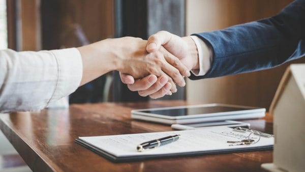 Two professionals shaking hands over a wooden table, signifying a successful agreement, likely related to selling a 1031 exchange property. On the table, there's a contract with a pen on top, indicating that a significant transaction has been completed. This could represent the finalization of the sale of a property under a 1031 exchange, a critical moment in the investment process.